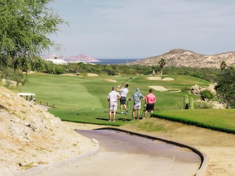 Golfers on a desert course with the sea beyond